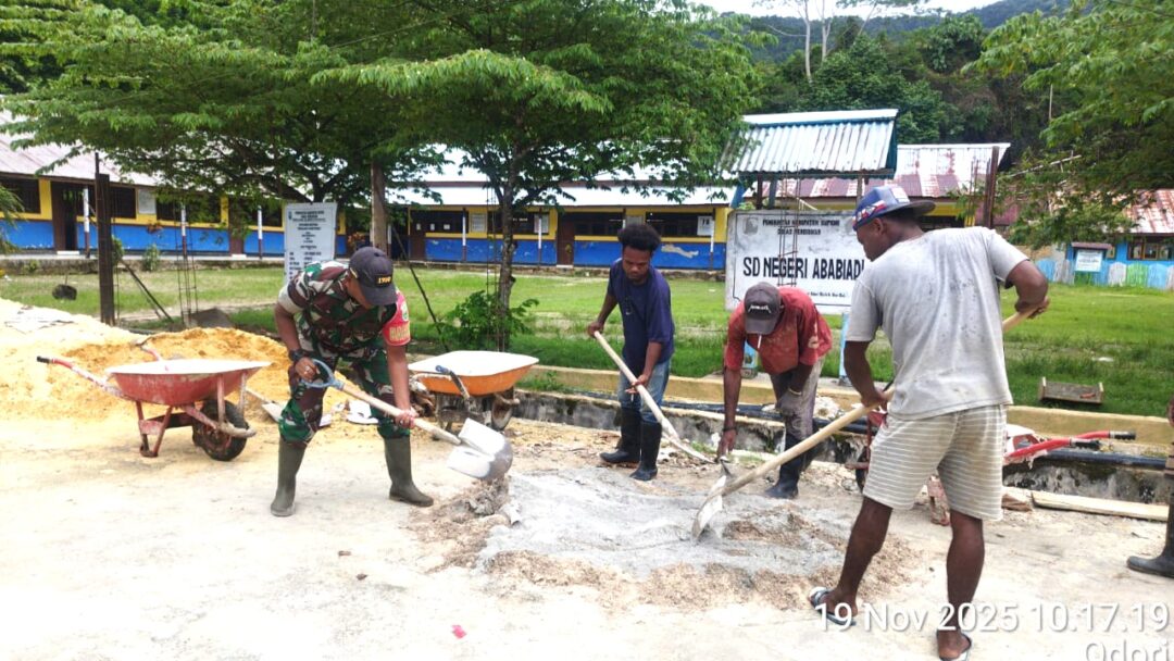 Babinsa Supiori Selatan Bantu Warga Campur Semen Pembangunan Pagar SD