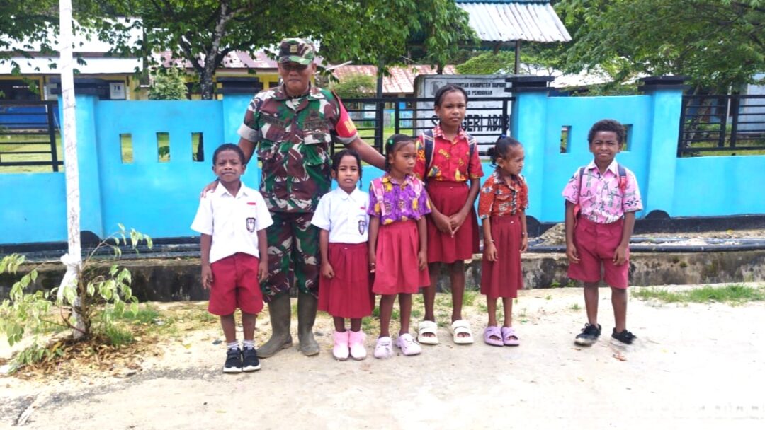 Babinsa Supiori Selatan Bantu Menyeberangi Anak Sekolah di Jalan Raya