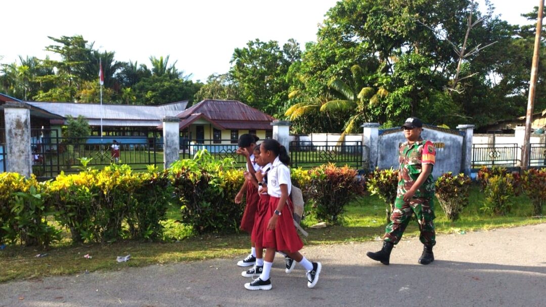Babinsa Supiori Selatan Bantu Anak Sekolah Menyeberang Jalan